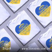 Футболка вчитель найкращого класу білого кольору, зображена з фронтального ракурсу на манекені, фон світло-сірий, принт у формі серця з жовто-блакитними кольорами та написом 'Вчитель найкращого класу у світі'.