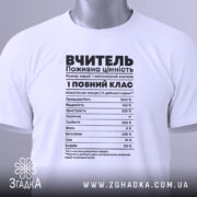 Футболка вчитель робочий заряд, біла, розкладена на поверхні, фон світло-сірий, принт чорного кольору з текстом про характеристики вчителя, на комірці зелена етикетка.