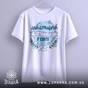 Футболка вчитель у світі, біла, зображена на манекені, фон світло-сірий, принт з написом 'НАЙКРАЩИЙ ВЧИТЕЛЬ У СВІТІ' у блакитному кольорі з елементами зелені.