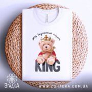 Футболка ведмежий король, білого кольору, складена на плетеній кошику, фон світлий, принт з ведмедиком у короні та червоному плащі, текст 'KING' великими літерами під ведмедиком.