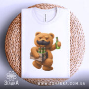 Футболка Ведмідь Пиво, складена футболка білого кольору, з принтом ведмедя з вусами, який тримає пляшку пива, на фоні плетеного кошика, деталі принта яскраві та чіткі.