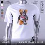 Футболка ведмідь термінатор, біла, зображена на манекені, фон світло-сірий, принт з ведмедем у сонцезахисних окулярах та механічною частиною, напис "НУ ЩО?" на червоному фоні.