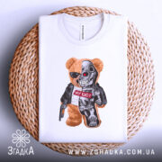 Футболка ведмідь термінатор, біла, складена на плетеній кошику, фон білий, принт з ведмедем у сонцезахисних окулярах та механічною частиною, напис "НУ ЩО?" на червоному фоні.