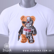 Футболка ведмідь термінатор, біла, складена на столі, фон світло-сірий, принт з ведмедем у сонцезахисних окулярах та механічною частиною, напис "НУ ЩО?" на червоному фоні, з етикеткою на зеленій стрічці.