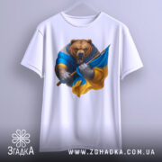 Футболка ведмідь Україна, біла, підвішена на вішалці, фон світло-сірий, принт ведмедя в синій та жовтій одежі, який тримає прапор України.