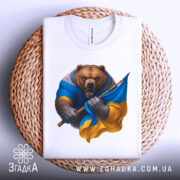 Футболка ведмідь Україна, біла, зображена на кошику, фон світло-сірий, принт ведмедя в синій та жовтій одежі, який тримає прапор України.