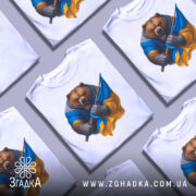 Футболка ведмідь Україна, біла, зображена на манекені, фон світло-сірий, принт ведмедя в синій та жовтій одежі, який тримає прапор України.