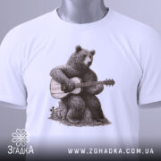 Футболка ведмідь з гітарою, біла, складена на поверхні, фон світло-сірий, принт з ведмедем, що грає на гітарі, на футболці є етикетка з логотипом.