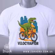 Футболка велоцираптор на велосипеді, біла, зображена з верхнього ракурсу, фон світлий, принт з велоцираптором на велосипеді, з тегом на шнурку, що підкреслює стиль.