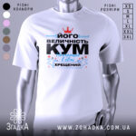 Футболка величність кум. Біла футболка на манекені, з принтом на грудях, що містить текст чорного та блакитного кольорів, а також червону корону. Фон світло-сірий, що підкреслює яскравість принта.