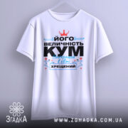 Футболка величність кум. Біла футболка на манекені, з принтом на грудях, що містить текст чорного та блакитного кольорів, а також червону корону. Фон світло-сірий, що підкреслює яскравість принта.