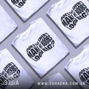 Футболка великі груди, біла, зображена на манекені з правого боку, фон світло-сірий, принт чорний з текстом 'DOES THIS SHIRT MAKE MY BOOBS LOOK BIG?' у центрі.