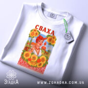 Футболка весела сваха, біла, зображена в складеному вигляді, фон світло-сірий, принт з жінкою в українському національному вбранні, соняшники навколо, напис 'СВАХА' червоним кольором, на комірці видна етикетка.