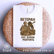 Футболка ветеран Бог війни, біла, складена на плетеній основі, фон світло-сірий, принт з військовим в бронежилеті та танком, текст коричневого кольору, видно етикетку на горловині.