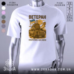 Футболка мужність України, біла, зображена з фронтального ракурсу, фон нейтральний, принт з чоловіком у військовій формі, що тримає прапор України, текст "ВЕТЕРАН" та "ПОВЕРНУВСЯ, ЩОБ ЖИТИ" вгорі та внизу принта.