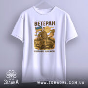 Футболка мужність України, біла, зображена з бокового ракурсу, фон світлий, принт з чоловіком у військовій формі, що тримає прапор України, текст "ВЕТЕРАН" та "ПОВЕРНУВСЯ, ЩОБ ЖИТИ" вгорі та внизу принта.