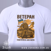 Футболка мужність України, біла, зображена з верхнього ракурсу, фон світлий, принт з чоловіком у військовій формі, що тримає прапор України, текст "ВЕТЕРАН" та "ПОВЕРНУВСЯ, ЩОБ ЖИТИ" розміщений під принтом, на футболці є етикетка.