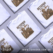 Футболка ветеран білого кольору, зображена на манекені, ракурс спереду, фон градієнтний сірий, принт з військовим, що тримає гвинтівку, з елементами природи та українським прапором на формі.