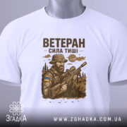 Футболка ветеран білого кольору, складена на поверхні, ракурс зверху, фон світлий, принт з військовим, що тримає гвинтівку, з елементами природи та українським прапором, з етикеткою на рукаві.