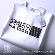 Футболка віддаюсь роботі, біла, розкладена на поверхні, фон світло-сірий, принт чорного кольору з текстом про відсотки на дні тижня, з зеленим ярликом.