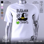 Футболка відьми не старіють, білого кольору, зображена з фронтального ракурсу на манекені, фон нейтральний, принт містить чорну відьомську шапку, зелену колбу з отрутою та текст.