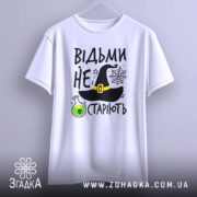 Футболка відьми не старіють, білого кольору, зображена з фронтального ракурсу, фон світло-сірий, принт містить чорну відьомську шапку, зелену колбу з отрутою та текст.