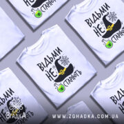 Футболка відьми не старіють, білого кольору, зображена з фронтального ракурсу на манекені, фон нейтральний, принт містить чорну відьомську шапку, зелену колбу з отрутою та текст.