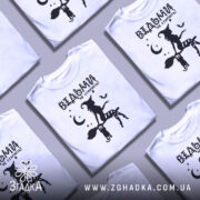 Футболка відьми не старіють, біла, зображена на манекені, фон світло-сірий, принт чорного кольору з відьмою на мітлі та котом, зірки та місяць навколо.