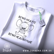 Футболка вєчно надуте, білого кольору, зображена в плоскому вигляді, фон світлий, принт з малюнком мишеняти з сердитим виразом обличчя та написом 'вєчно недовольне', на комірці прикріплена етикетка.