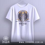 Футболка вікінги одін, біла, підвішена на вішалці, фон світло-сірий, принт з вікінгом, шоломом та мечами, текст 'VIKINGS' під малюнком.