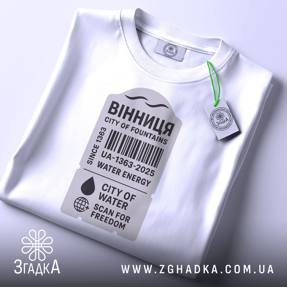 Футболка Вінниця місто фонтанів, біла, складена на поверхні, фон світло-сірий, принт у сірому кольорі з текстом "ВІННИЦЯ CITY OF FOUNTAINS" та етикетка з зеленим шнурком.