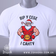 Футболка вір у себе і санту, білого кольору, складена на поверхні, фон світло-сірий, принт з Сантою в червоному костюмі, з написом 'ВІР У СЕБЕ І САНТУ' та зеленим ярликом.