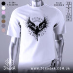 Футболка вісник одіна, біла, зображена з фронтального ракурсу, на манекені, фон світло-сірий, принт чорного кольору з крилами та написом 'VІСНІК ОДІНА'.