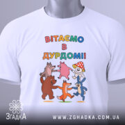 Футболка вітаємо в дурдомі, біла, зображена зверху, на фоні світло-сірого кольору, принт з веселими персонажами, які танцюють, з написом 'ВІТАЄМО В ДУРДОМІ!!', на футболці також є етикетка з зеленим шнурком.