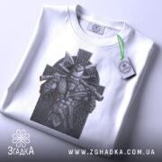 Футболка воїн вікінг білого кольору, складена на столі, зображення вікінга з сокирами на фоні кельтського хреста, видно етикетку з логотипом бренду.