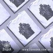 Футболка воїн вікінг білого кольору, зображена з фронтального ракурсу на манекені, фон світло-сірий, принт зображає потужного вікінга з сокирами на фоні кельтського хреста.