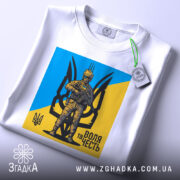 Футболка воля честь, біла, зображена на столі з легким ракурсом зверху, фон світло-сірий, принт з жовто-блакитним фоном та зображенням персонажа в військовій формі, з етикеткою на комірці.