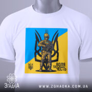 Футболка воля честь, біла, зображена на столі з легким ракурсом зверху, фон світло-сірий, принт з жовто-блакитним фоном та зображенням персонажа в військовій формі, з етикеткою на комірці.