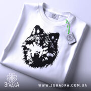 Футболка вовчий погляд, біла, складена на плоскій поверхні, фон світло-сірий, принт чорного кольору з зображенням голови вовка, на комірці видна етикетка.