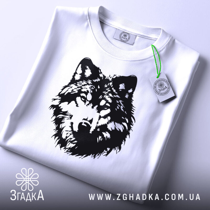 Футболка вовчий погляд, біла, складена на плоскій поверхні, фон світло-сірий, принт чорного кольору з зображенням голови вовка, на комірці видна етикетка.