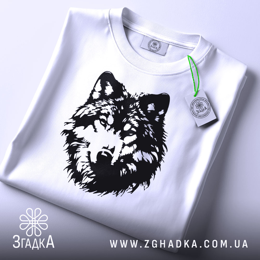Футболка вовчий погляд, біла, складена на плоскій поверхні, фон світло-сірий, принт чорного кольору з зображенням голови вовка, на комірці видна етикетка.
