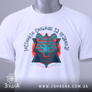 Футболка вовк інстинкти, складена біла футболка з принтом, ракурс зверху, фон світло-сірий, принт зображає вовка в геометричному стилі, текст 'ІНСТИНКТИ СИЛЬНІШІ ЗА ПРАВИЛА!' з яскравими кольорами.