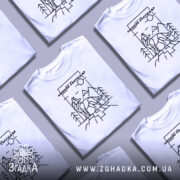 Футболка вовк лісовий господар, біла, зображена з фронтального ракурсу на манекені, фон світло-сірий, принт з чорними лініями, що зображує вовка на фоні гір і дерев.