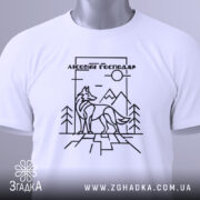 Футболка вовк лісовий господар, біла, складена на поверхні, зображена з верхнього ракурсу, фон світло-сірий, принт з чорними лініями, що зображує вовка на фоні гір і дерев, з етикеткою з зеленим шнурком.