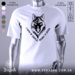 Футболка вовк у душі, біла, зображена на манекені, фон світлий, принт чорного кольору з зображенням вовка та написом 'Гори в серці, вовк у душі'.