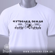 Футболка вождя нашого білого кольору, складена на поверхні, з принтом чорного кольору, з етикеткою зеленого кольору, на фоні світло-сірого градієнту, з чітким зображенням фігурок людей та слона.