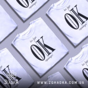 Футболка все буде ок, білого кольору, зображена з фронтального ракурсу на манекені, фон світлий, принт чорного кольору з великими літерами 'OK' та текстом 'все буде гарантію!' у верхній частині.