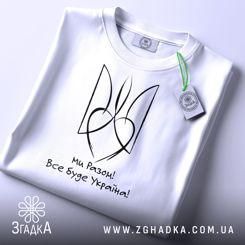 Футболка все буде Україна, біла, складена на столі, фон світло-сірий, принт чорного кольору з написом 'Ми Разом! Все буде Україна!' та стилізованим гербом, з етикеткою зеленого кольору.