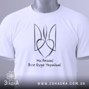 Футболка все буде Україна, біла, складена на столі, фон світло-сірий, принт чорного кольору з написом 'Ми Разом! Все буде Україна!' та стилізованим гербом, з етикеткою зеленого кольору.