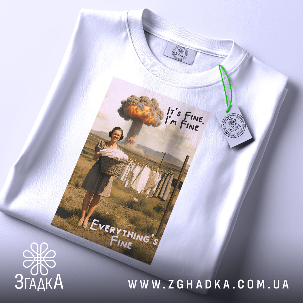 Футболка все під контролем. Білий колір, ракурс зверху, фон світлий. Принт з жінкою, яка тримає кошик з білизною, текст 'It's Fine, I'm Fine' та 'Everything's Fine', на ярлику зелена стрічка.